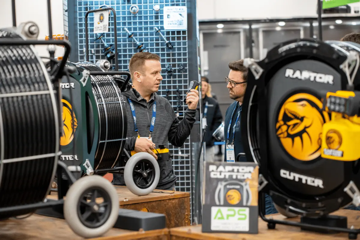 APS team member demonstrating the Raptor Cutter system to an attendee at a trade show, highlighting drain cleaning and pipe rehabilitation equipment