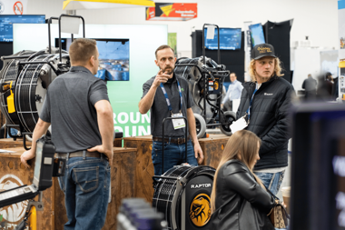 APS team member demonstrating a Raptor Cutter to attendees at a trenchless technology trade show, showcasing pipeline rehabilitation equipment and answering customer questions.